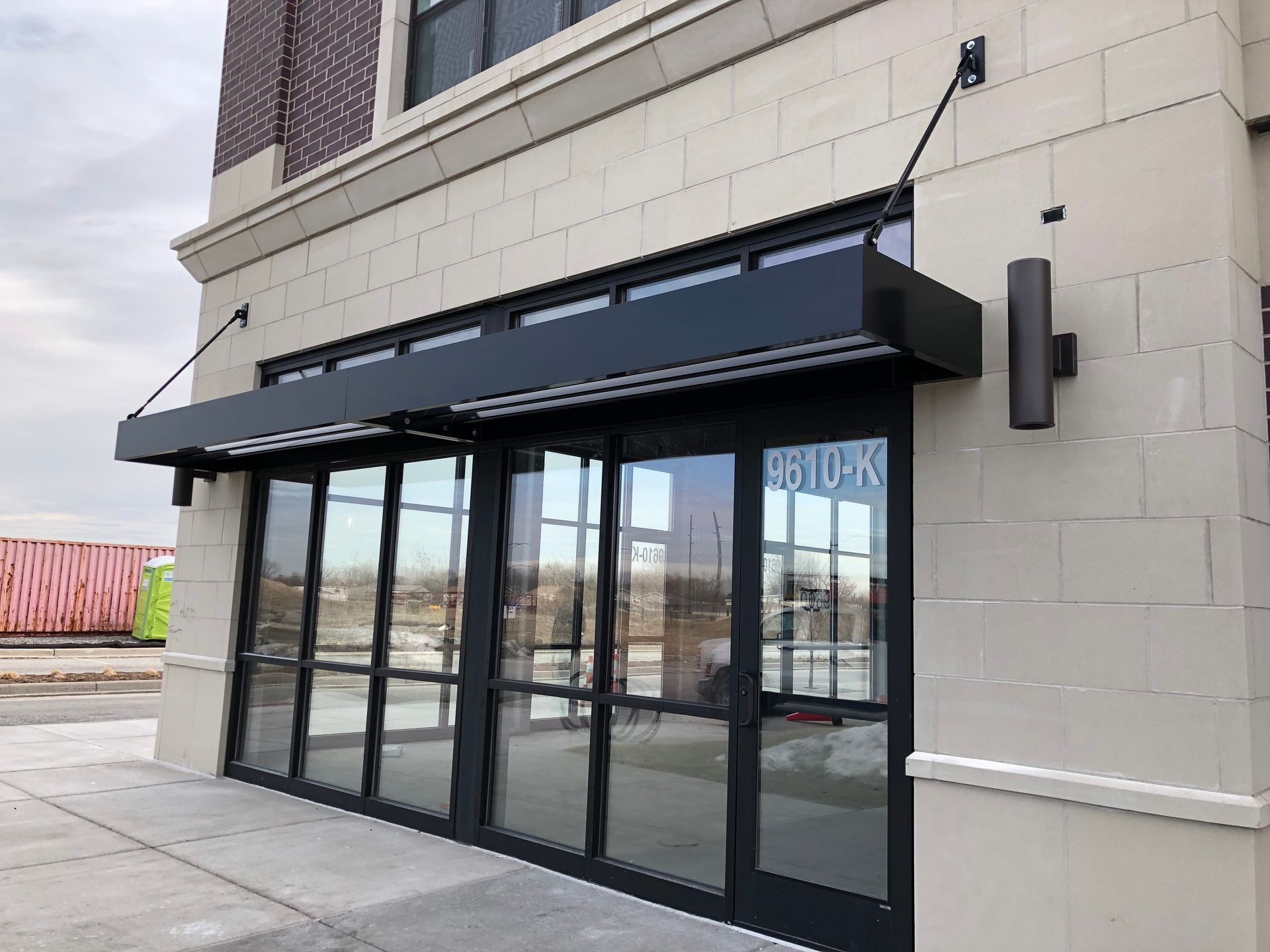 Storefront with black awning and glass doors on a beige building exterior