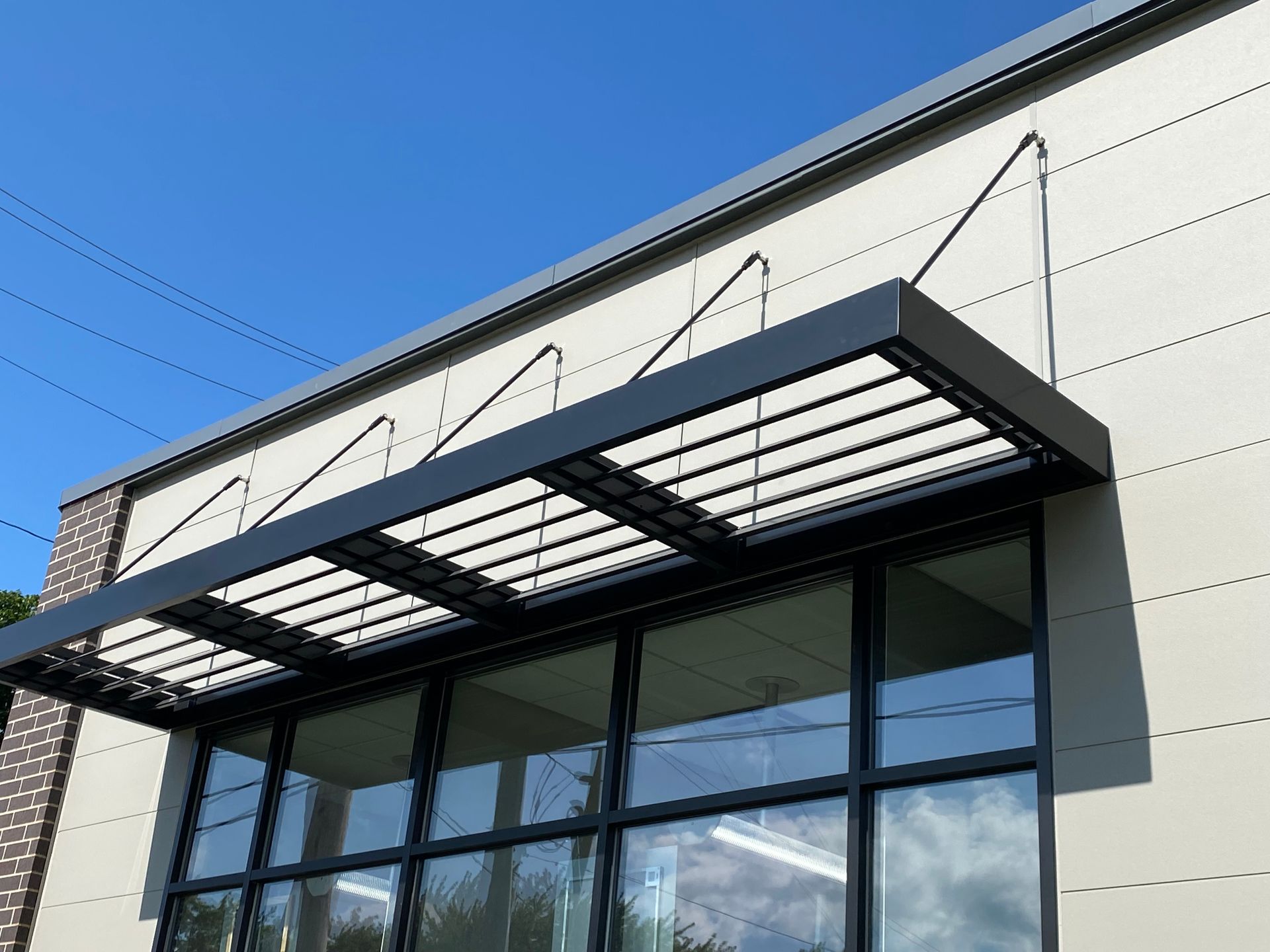 Modern building entrance with a black metal awning and large glass windows under a blue sky