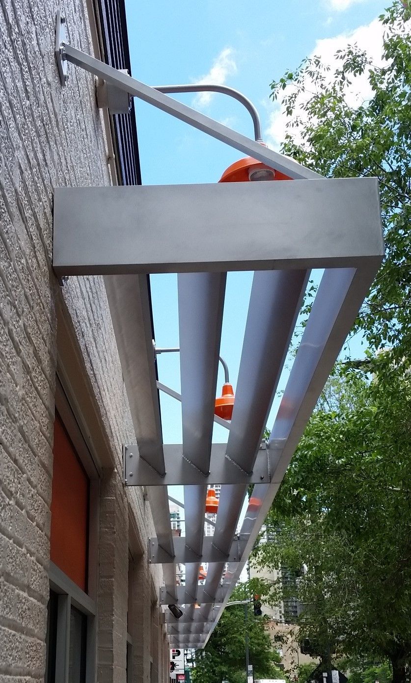Covered sidewalk with silver awning along a brick building, trees lining the street.