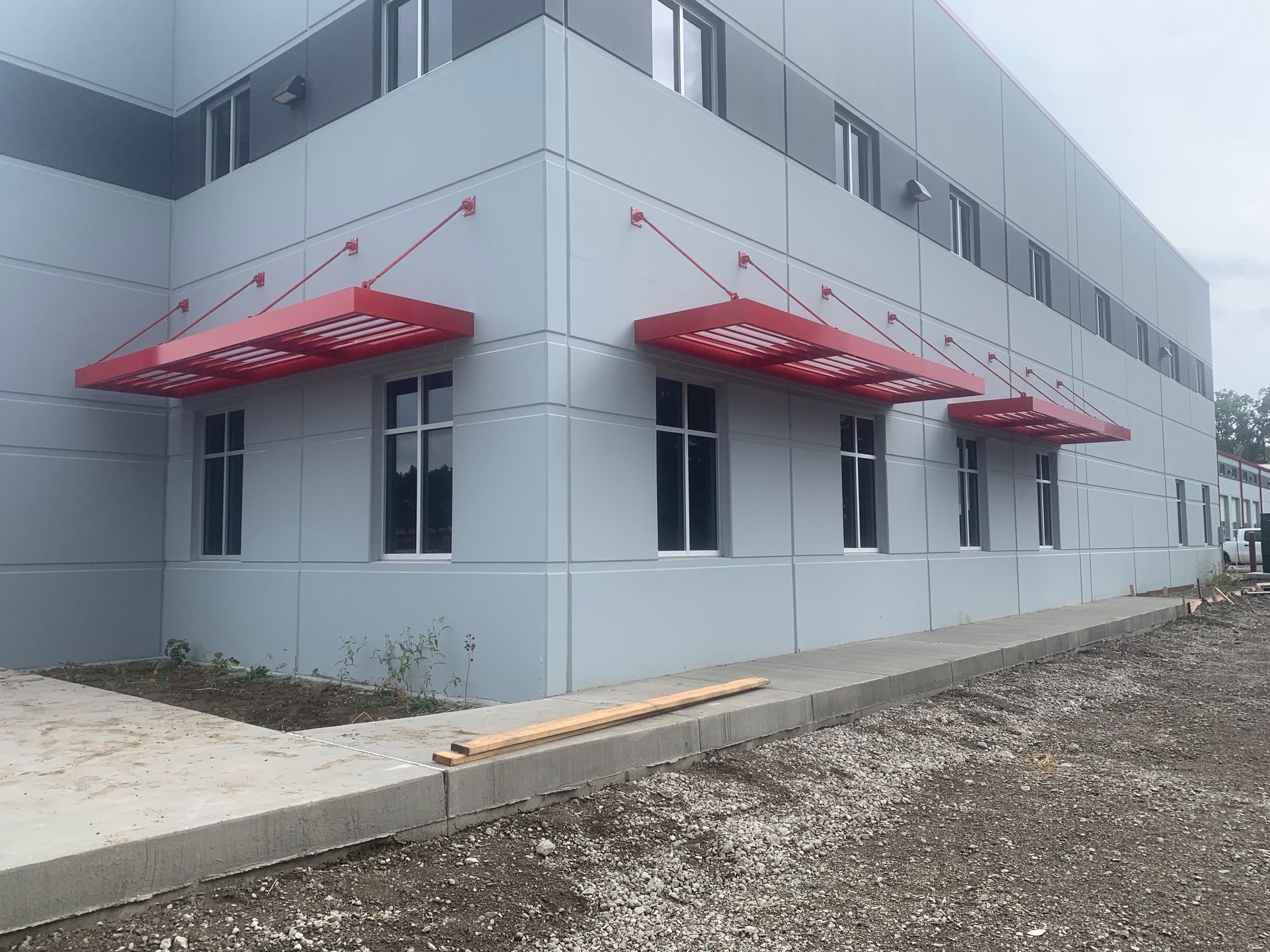 Gray commercial building with red awnings and small windows along a gravel lot
