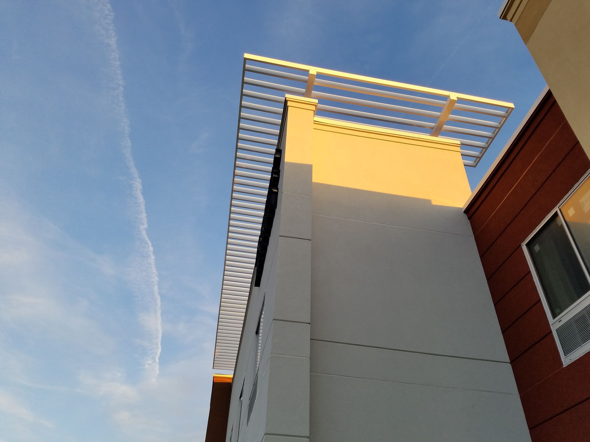 Low-angle view of a white building with a metal rooftop trellis against a blue sky.