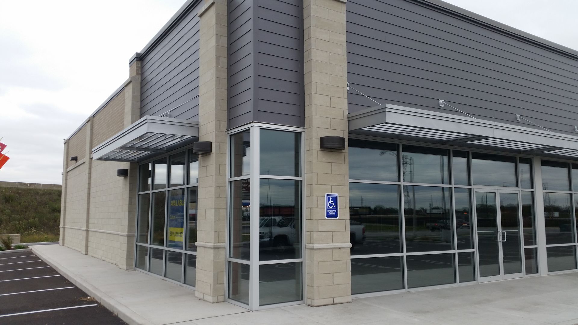 Modern storefront with glass doors and windows, gray siding, and accessible entrance parking space.