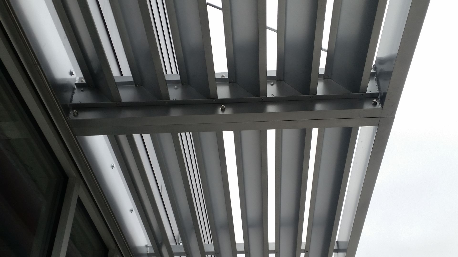 Underside of a metal bridge or overpass with gray beams against a cloudy sky