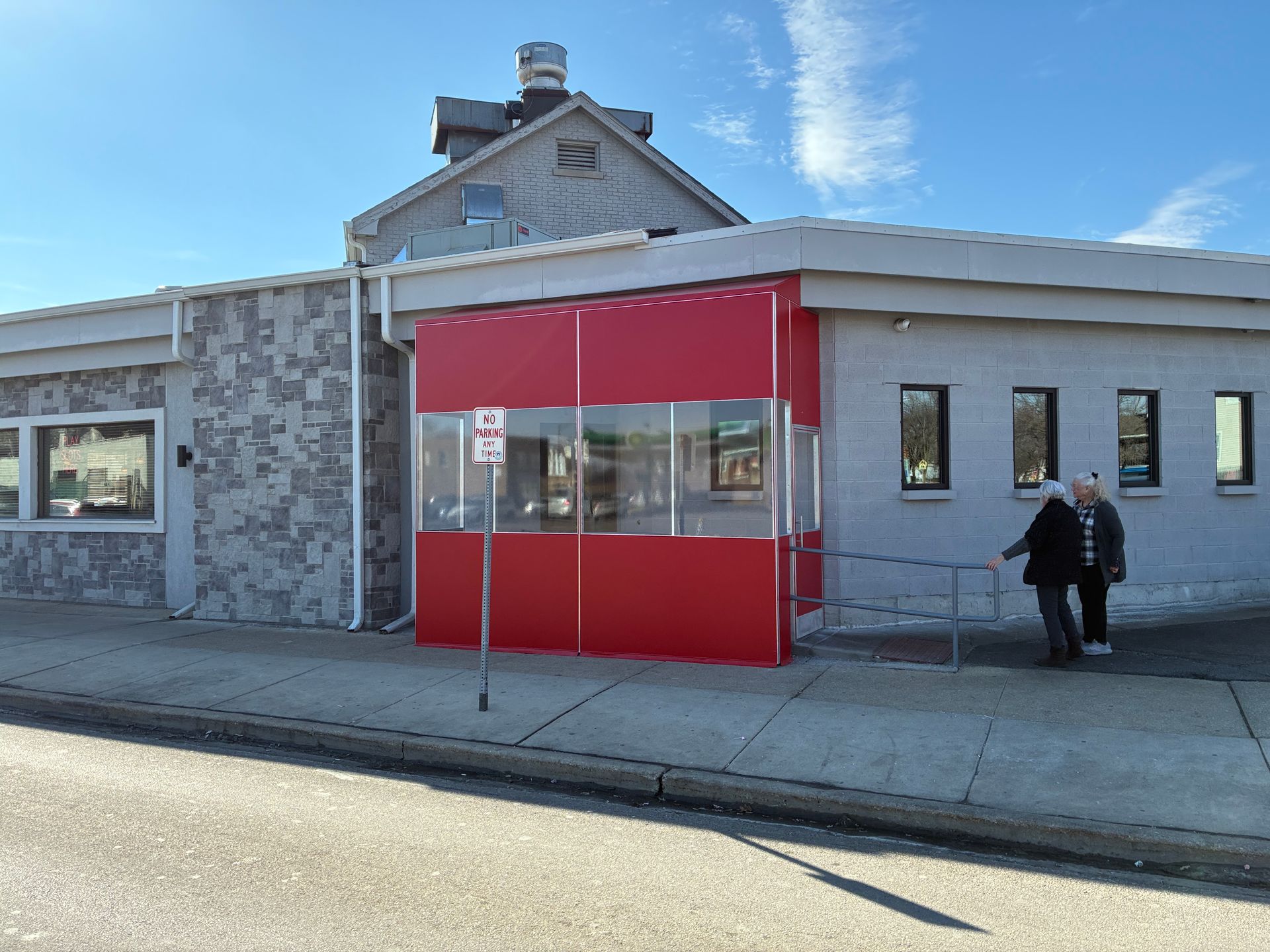 Red storefront entrance on a gray building with a person standing outside on the sidewalk.