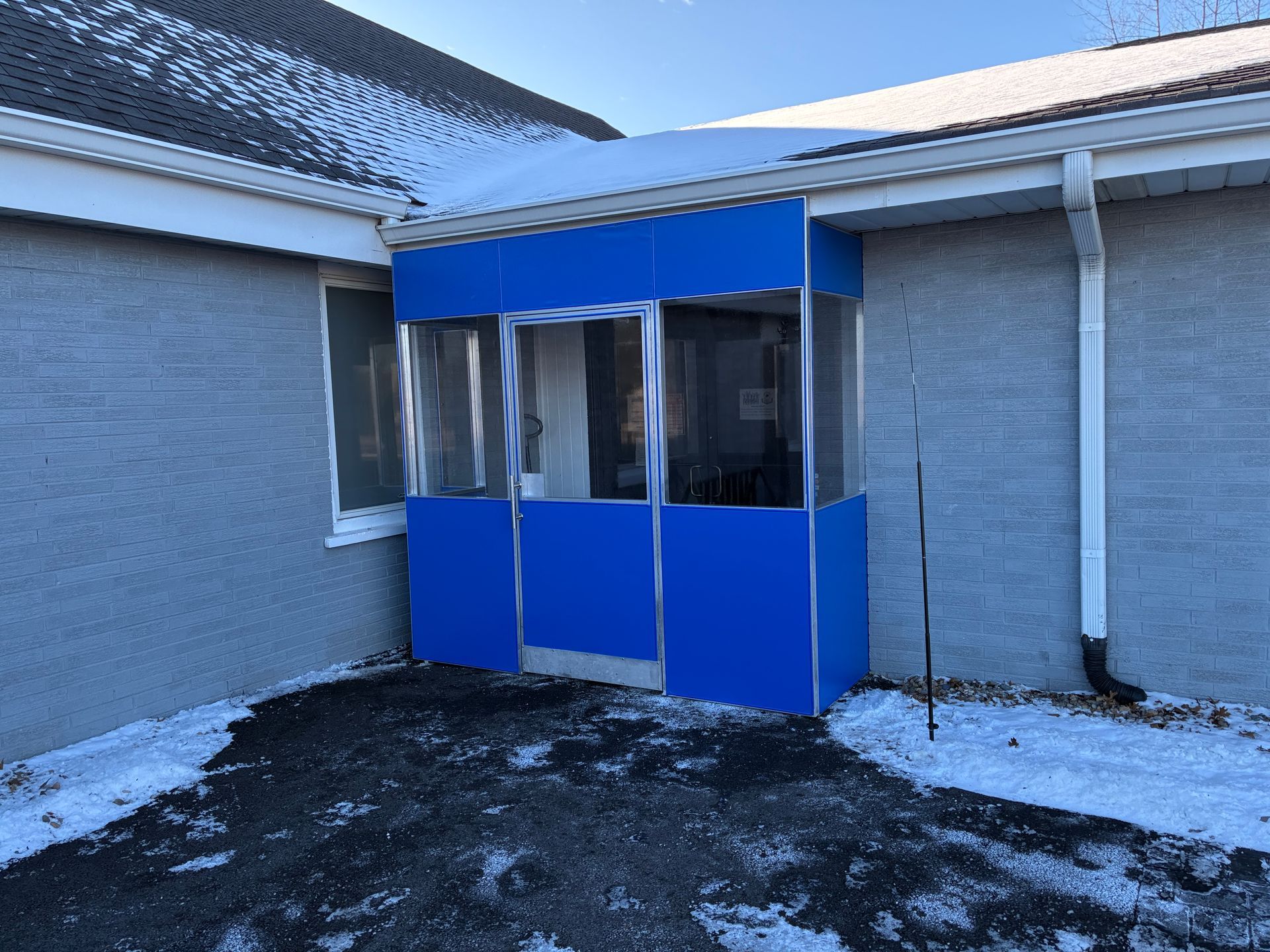 Blue enclosed entrance at a gray building with snow on the ground and roof.