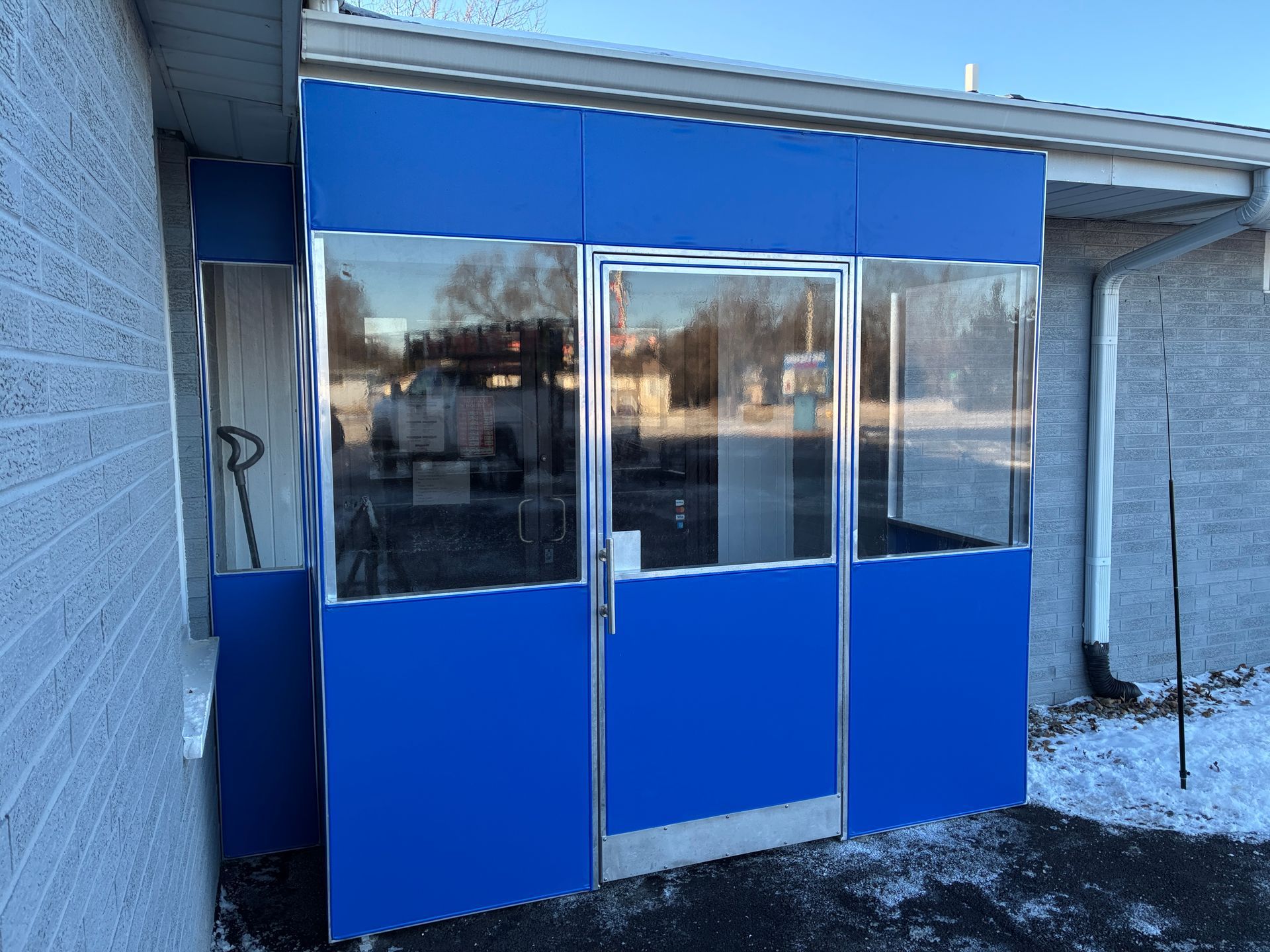 Blue glass entry vestibule attached to a building, with snowy ground outside.