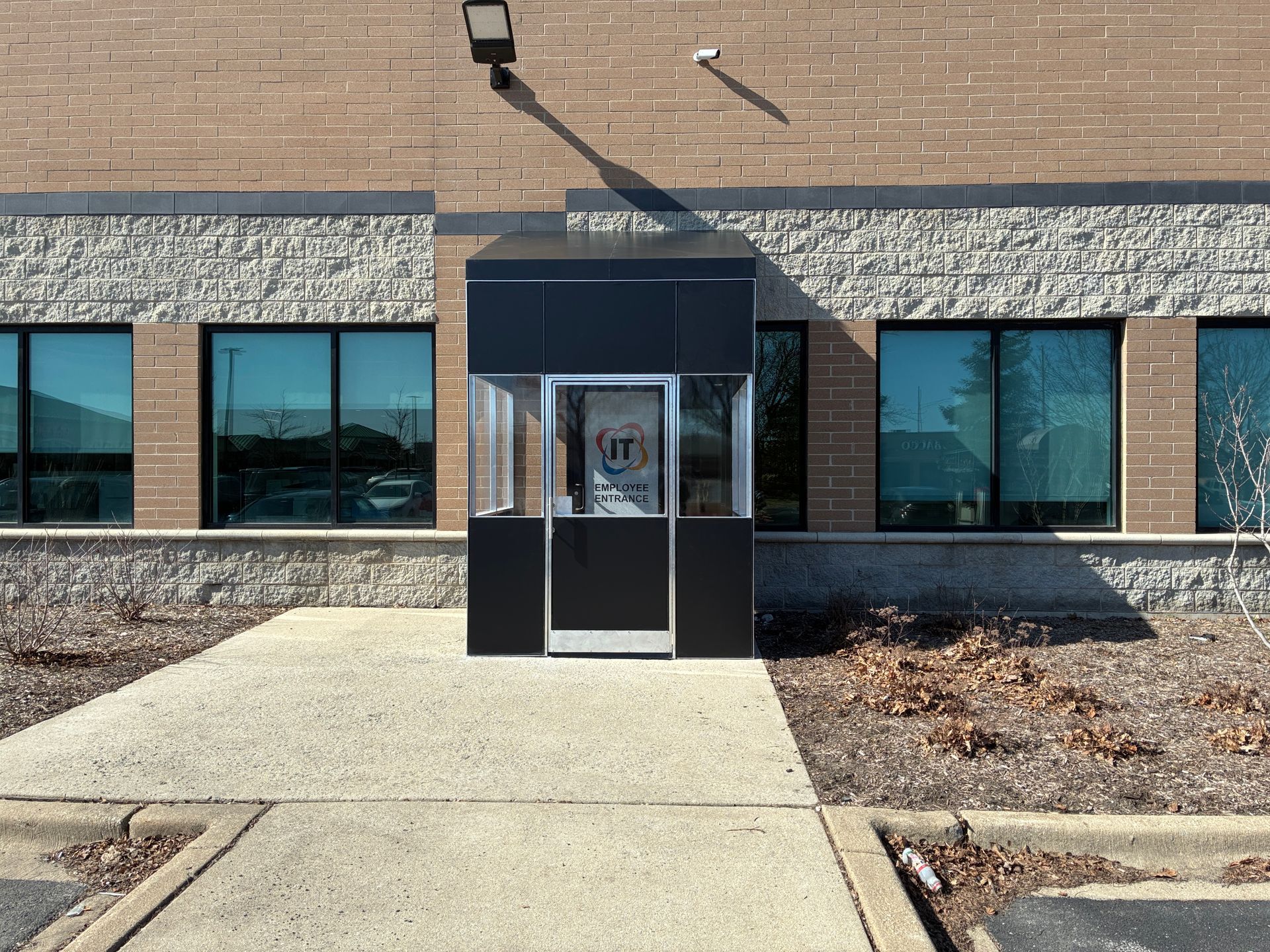 Front entrance to a brick building with a glass door, windows, and a concrete walkway.
