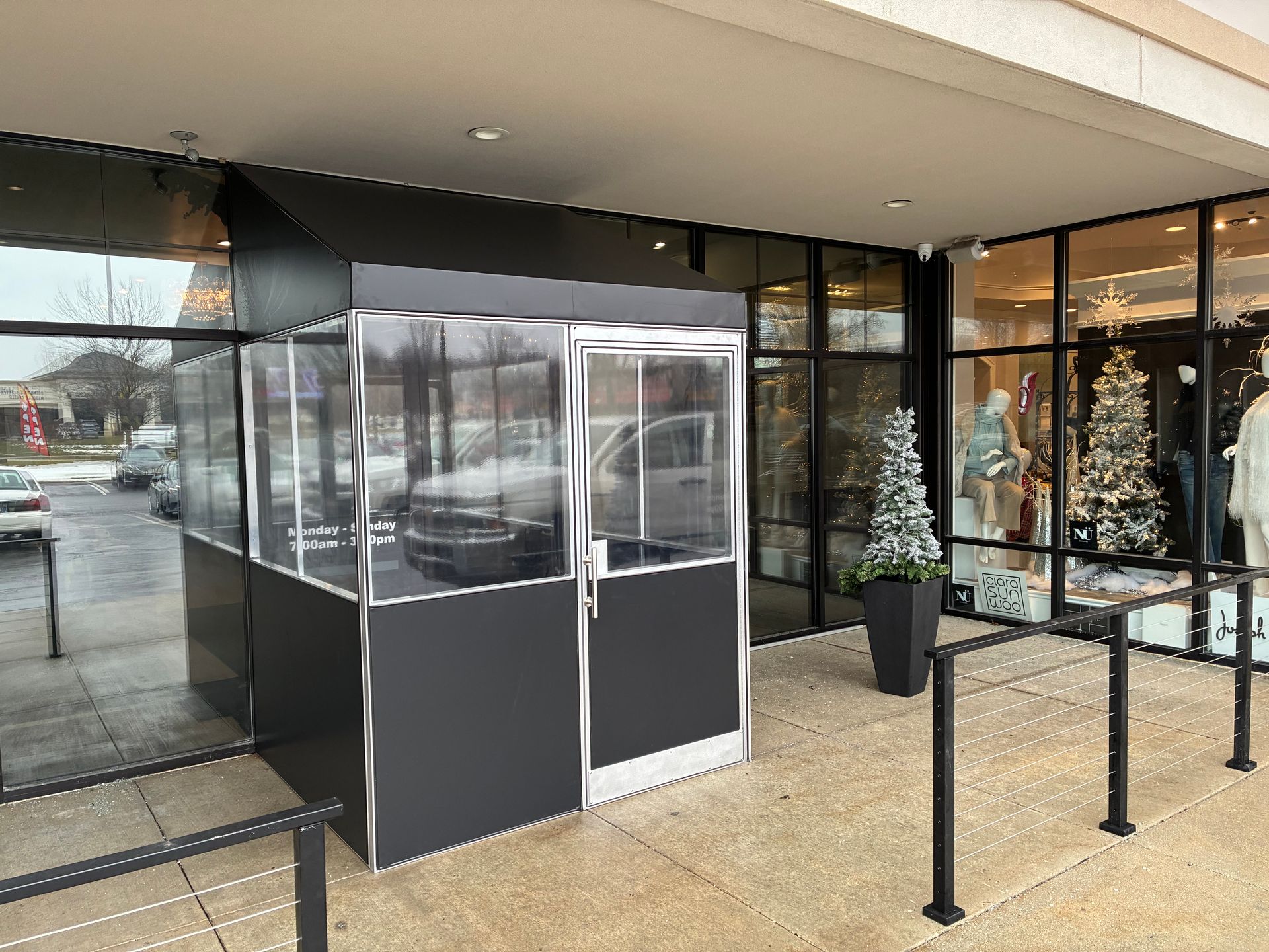 Covered storefront entrance with a glass vestibule and black railings on a snowy day