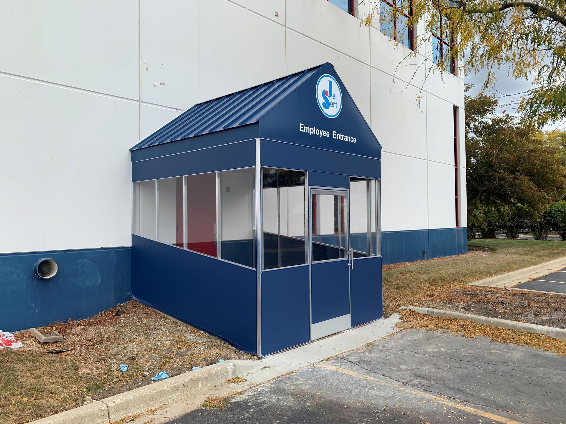 Blue awning entrance booth beside a white building with windows and a paved walkway