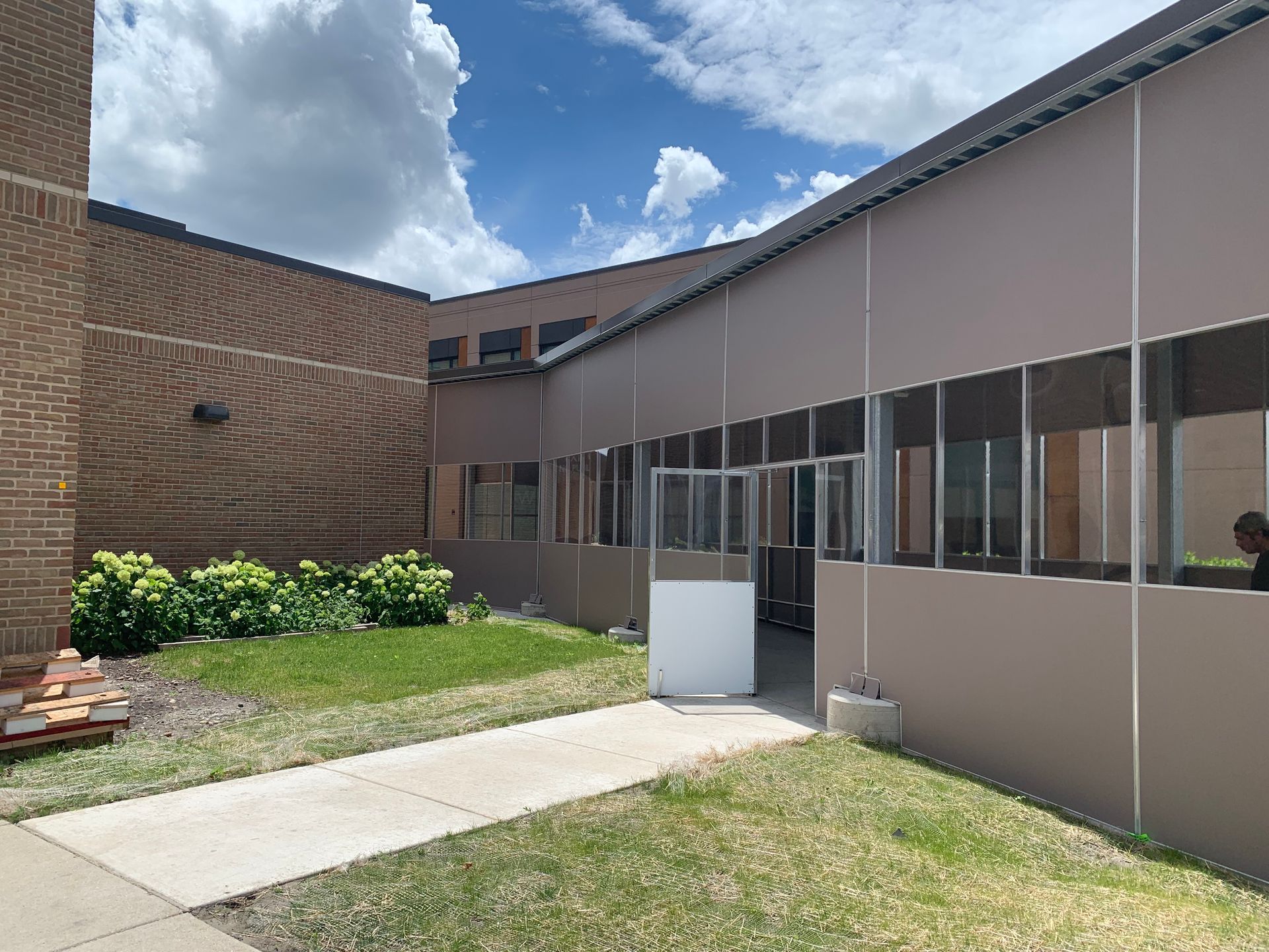 Courtyard between brick and beige buildings with grass, sidewalk, and cloudy sky
