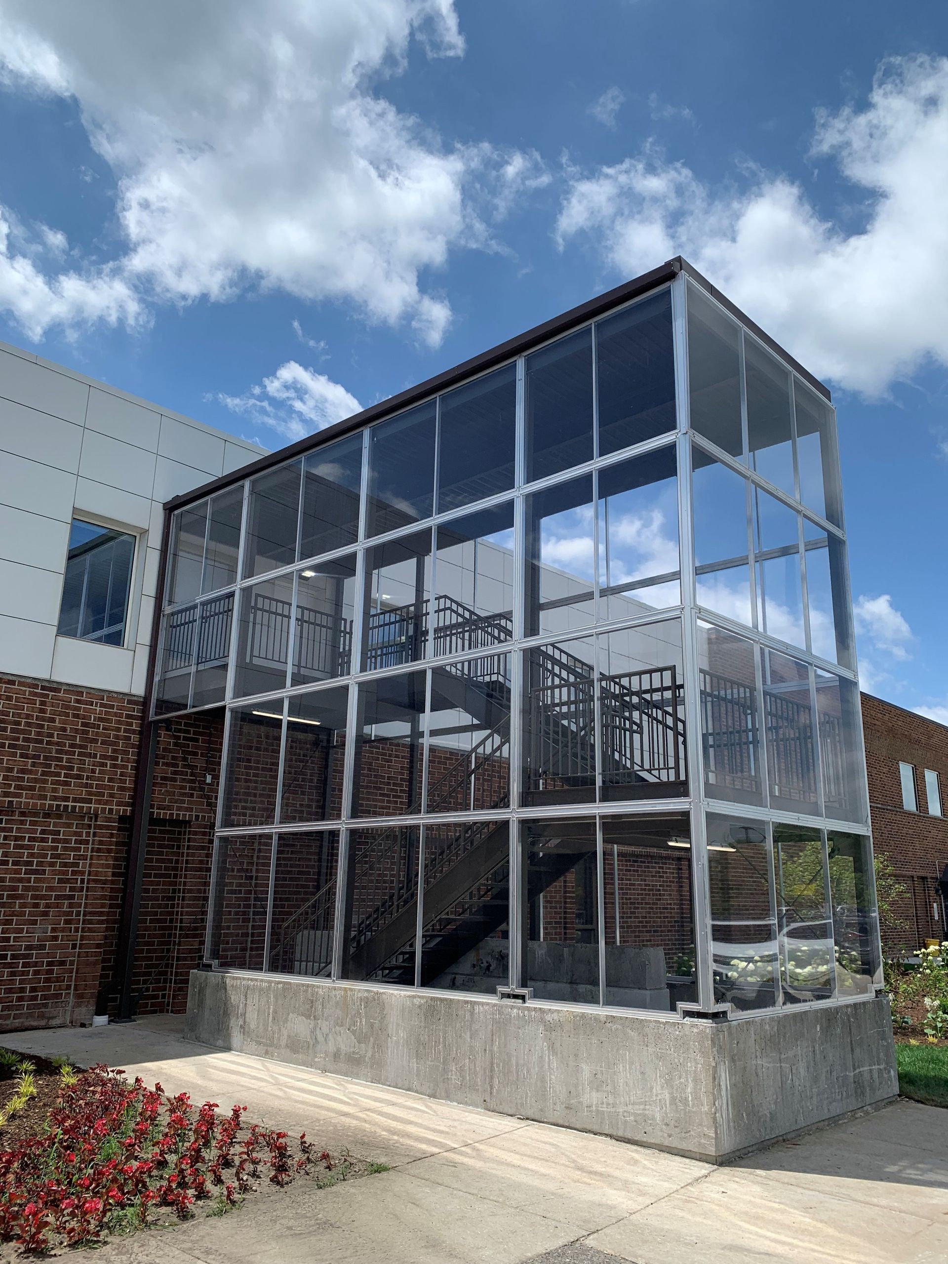 Glass-enclosed stair tower beside a brick building under a partly cloudy sky