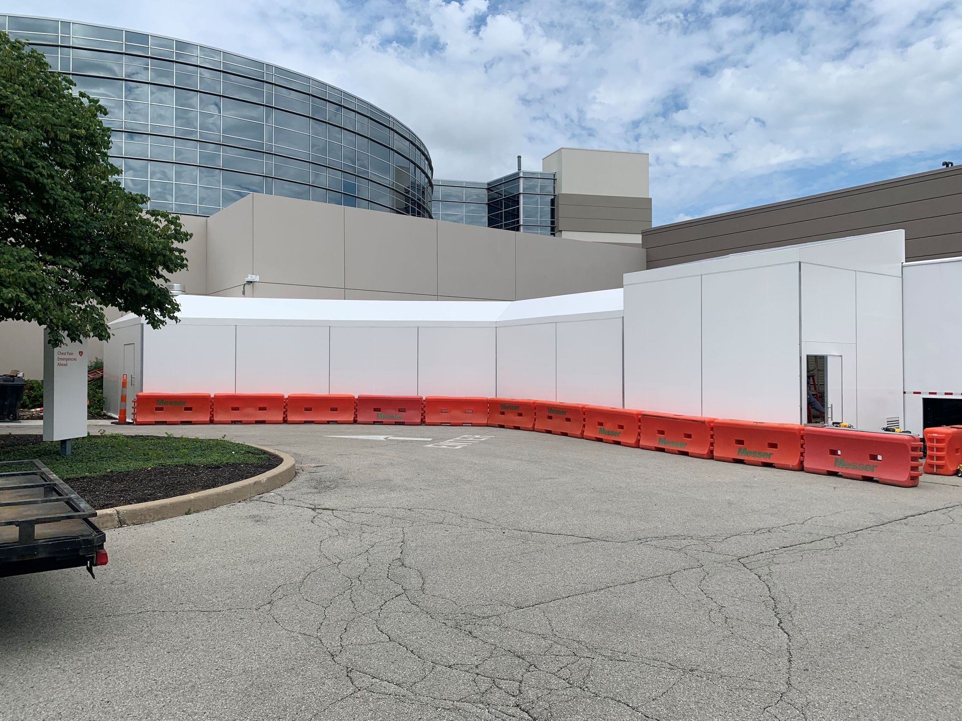 Orange barriers in front of a white building and curved glass facade on a paved lot