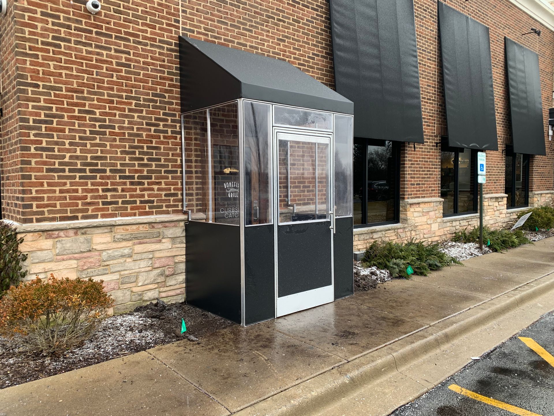 Clear outdoor phone booth beside a brick building on a wet sidewalk