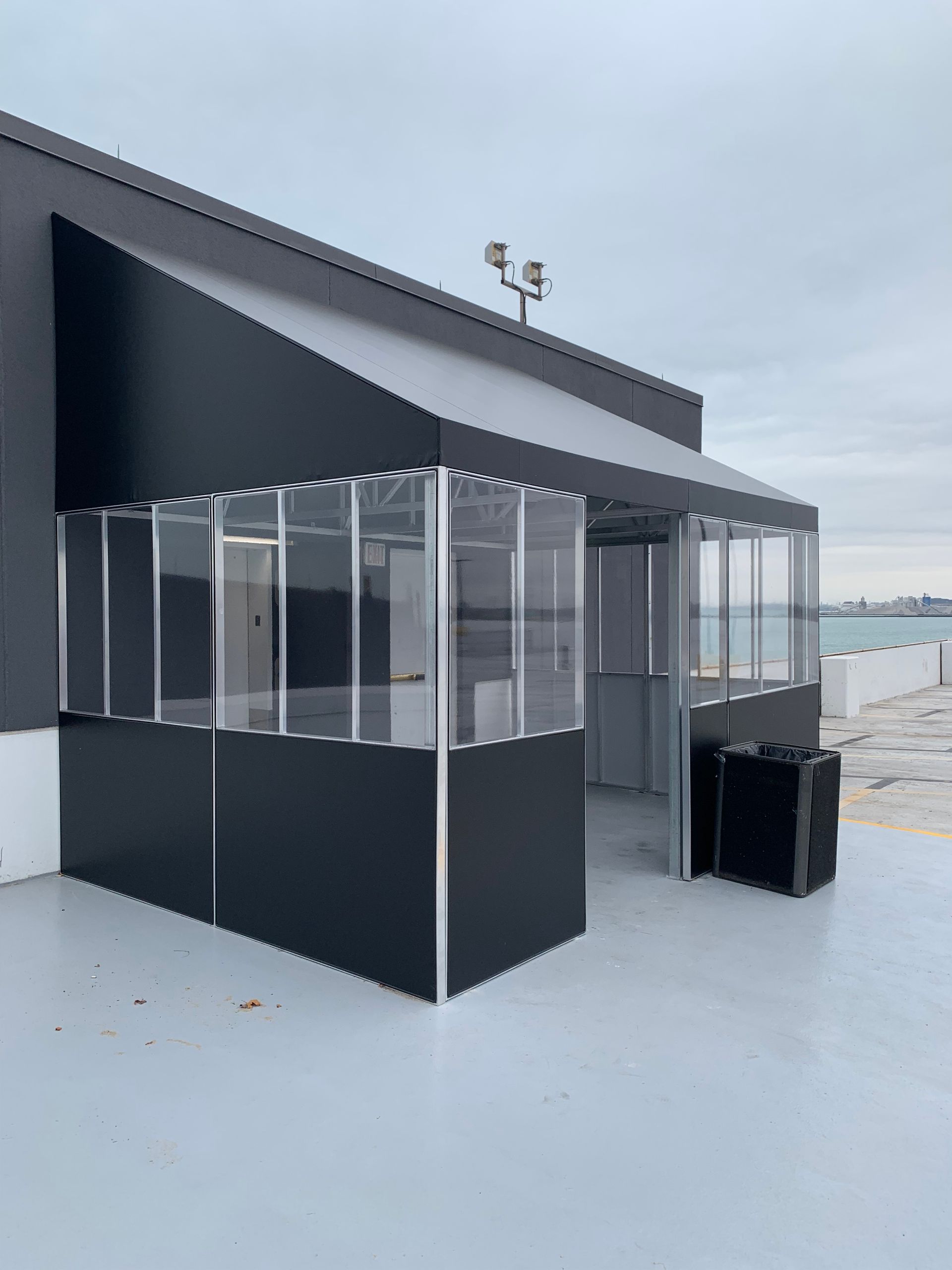 Black outdoor patio enclosure with clear vinyl panels beside a modern building on a rooftop terrace