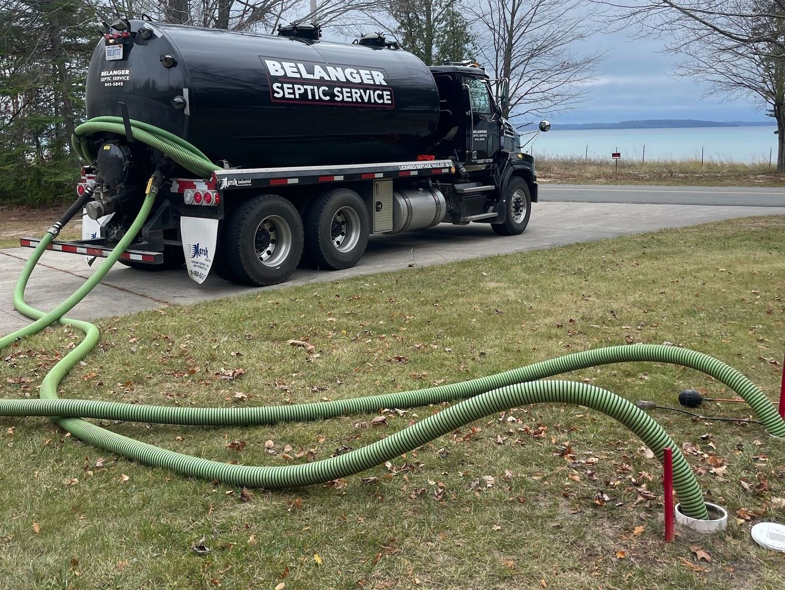 A septic truck is parked on the side of the road with green hoses attached to it.
