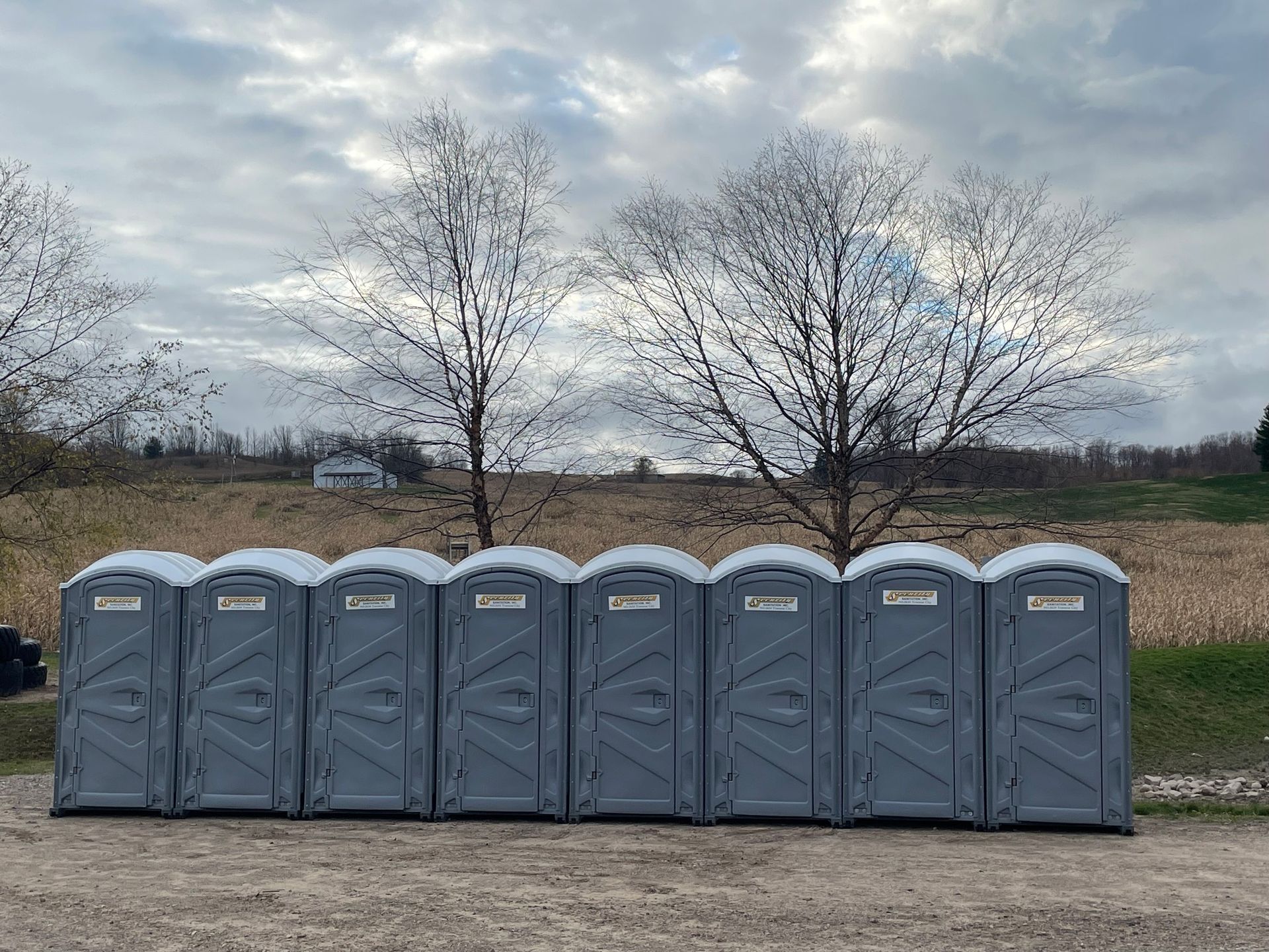 A row of portable toilets are lined up in a field.