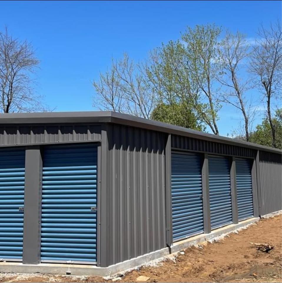 Storage units with blue rolling doors and gray metal siding, under a bright blue sky.
