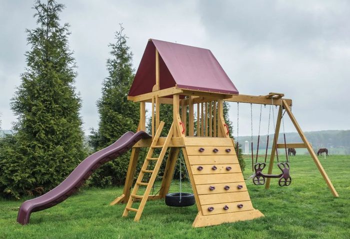 A wooden playground set with a slide and swings in a grassy field