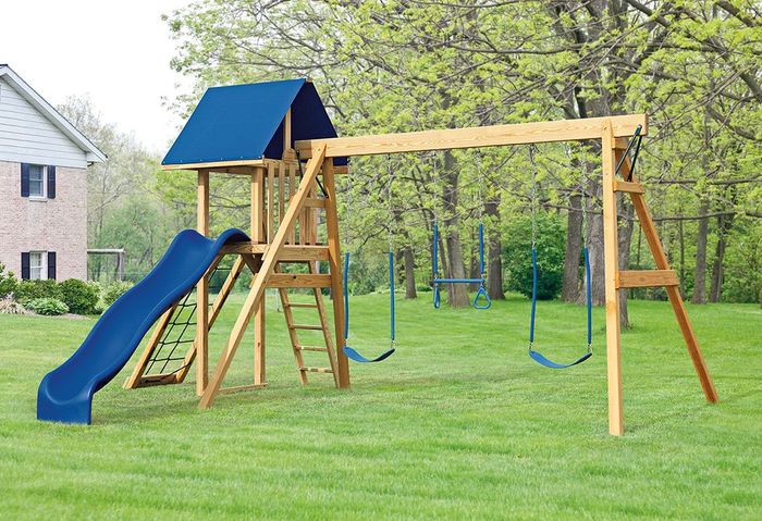 A wooden playground set with a blue slide and swings in a lush green yard