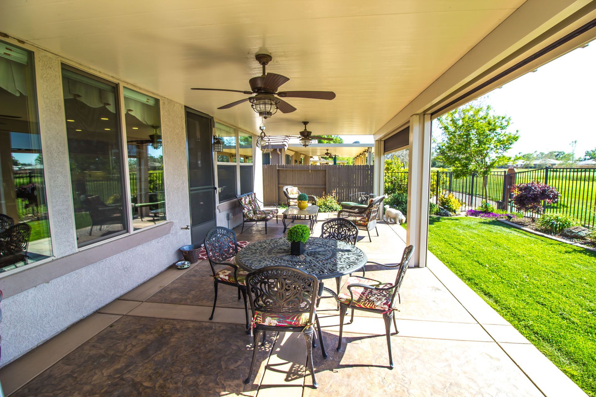 Covered patio with dining set, overlooking a green lawn and garden.