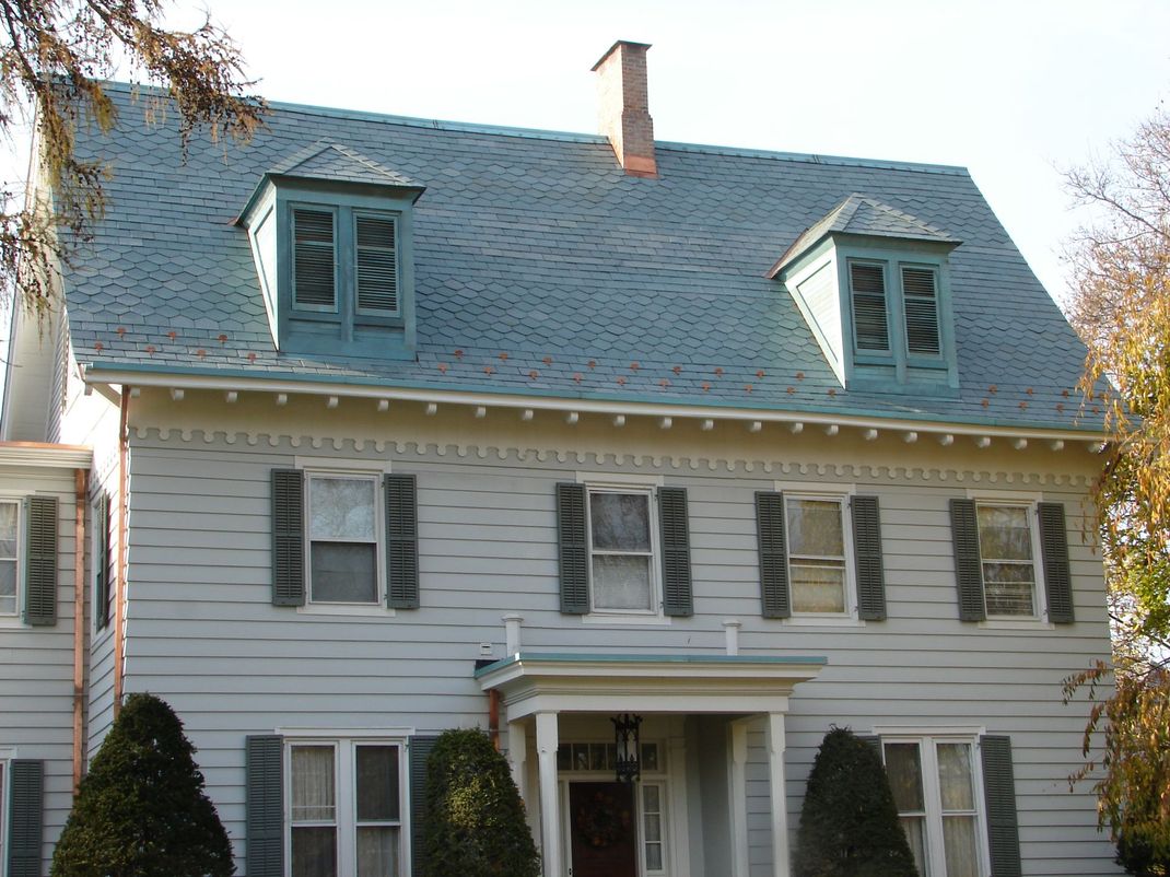 Two-story white house with blue roof, dormer windows, and a small front porch