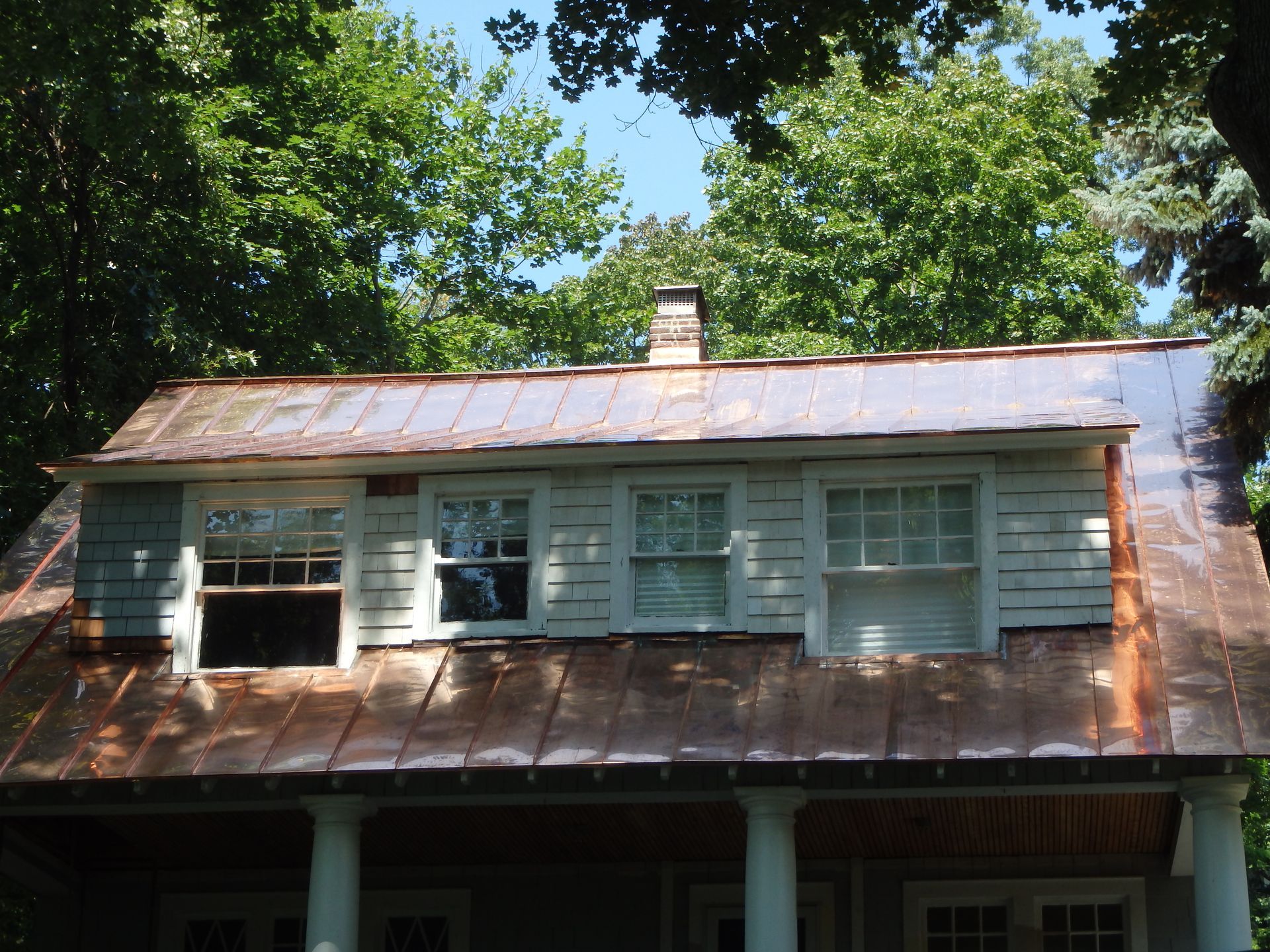 Rustic house with weathered metal roof and white shutters, surrounded by tall green trees