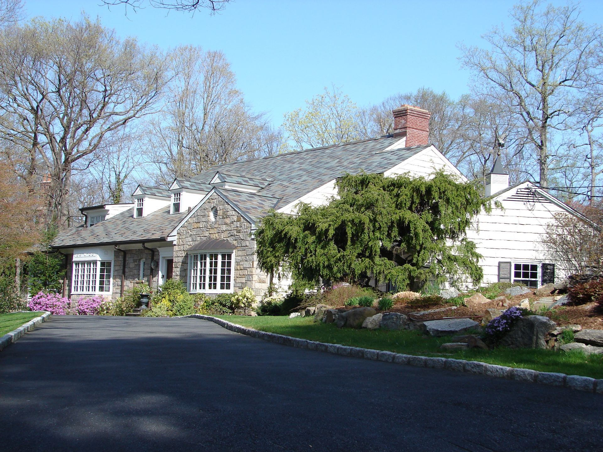 Suburban house with a gray roof, front garden, and a driveway under a clear blue sky