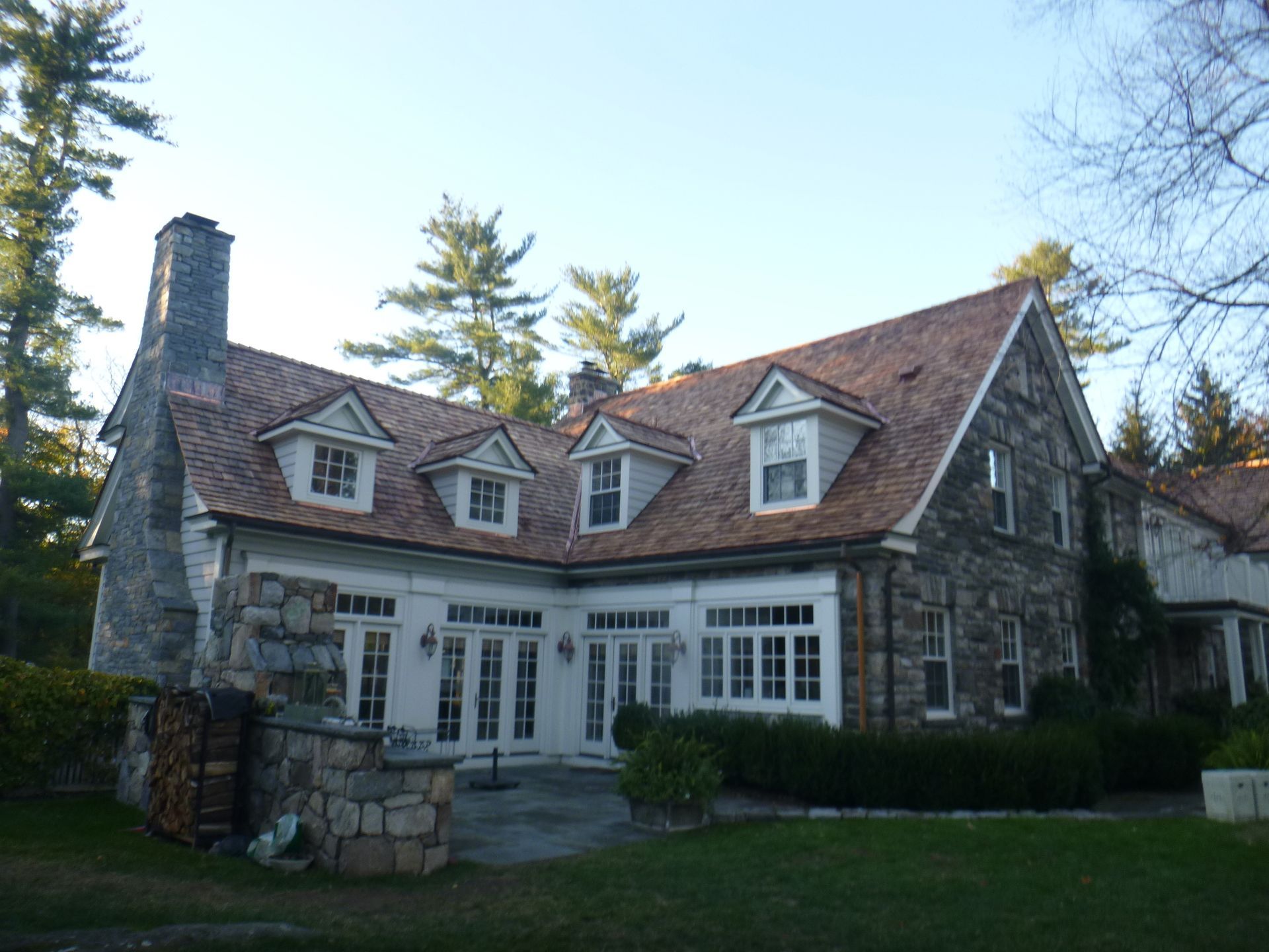 Stone house with red roof and dormer windows, surrounded by trees and lawn.