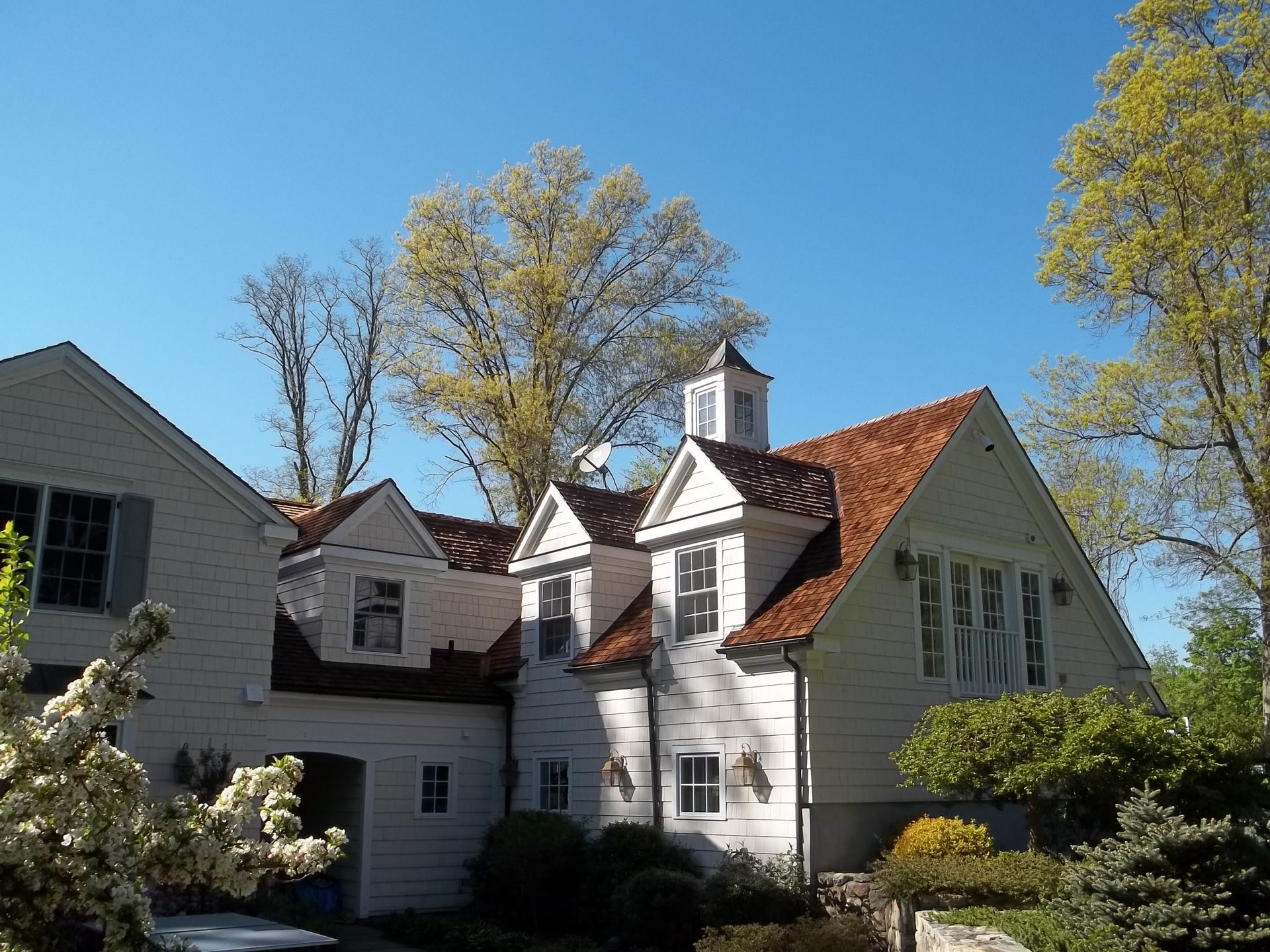 White house with red roof and dormer windows surrounded by autumn trees under a clear blue sky