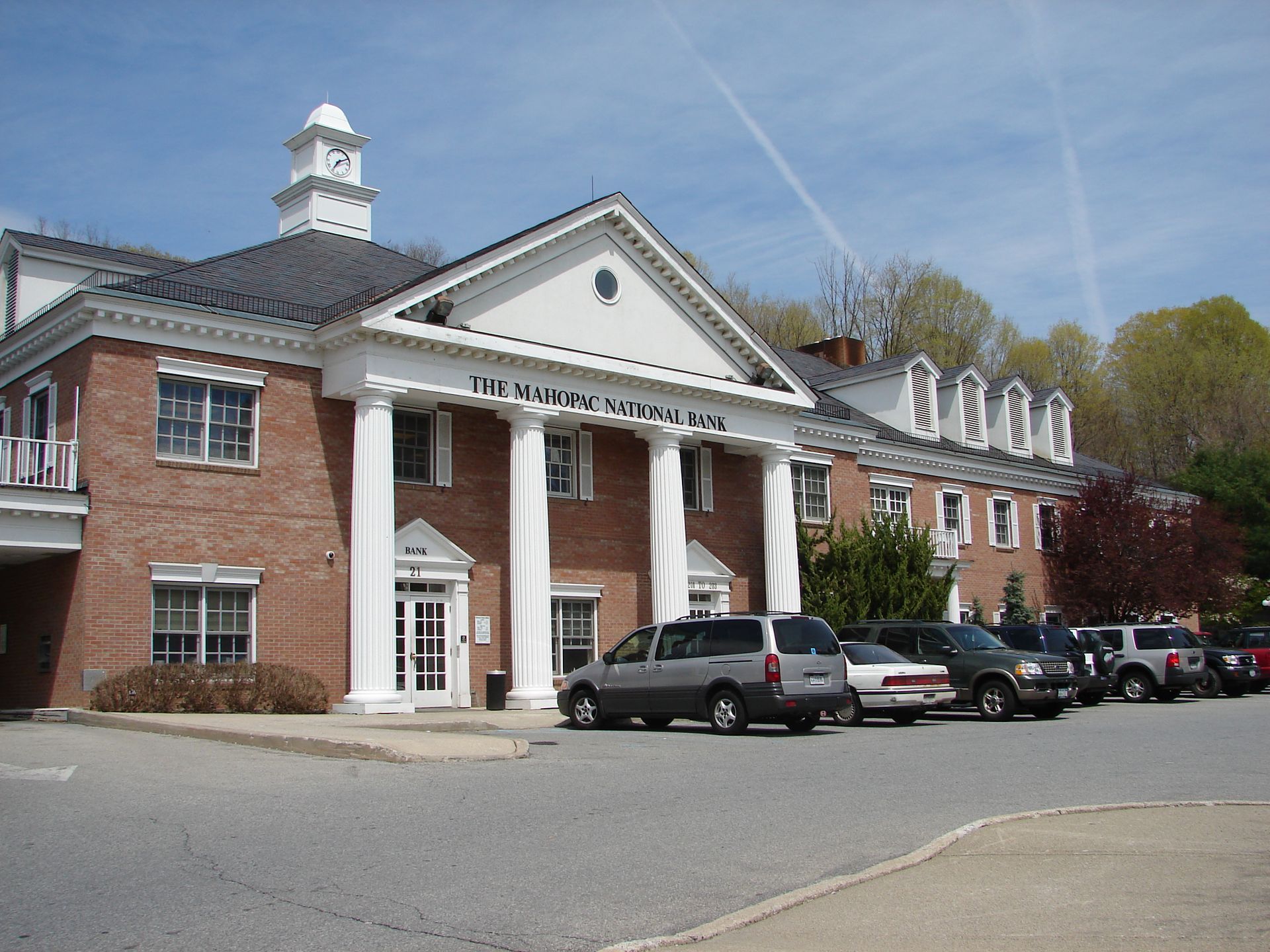 Brick civic building with white columns and cupola, parked cars in front under a blue sky