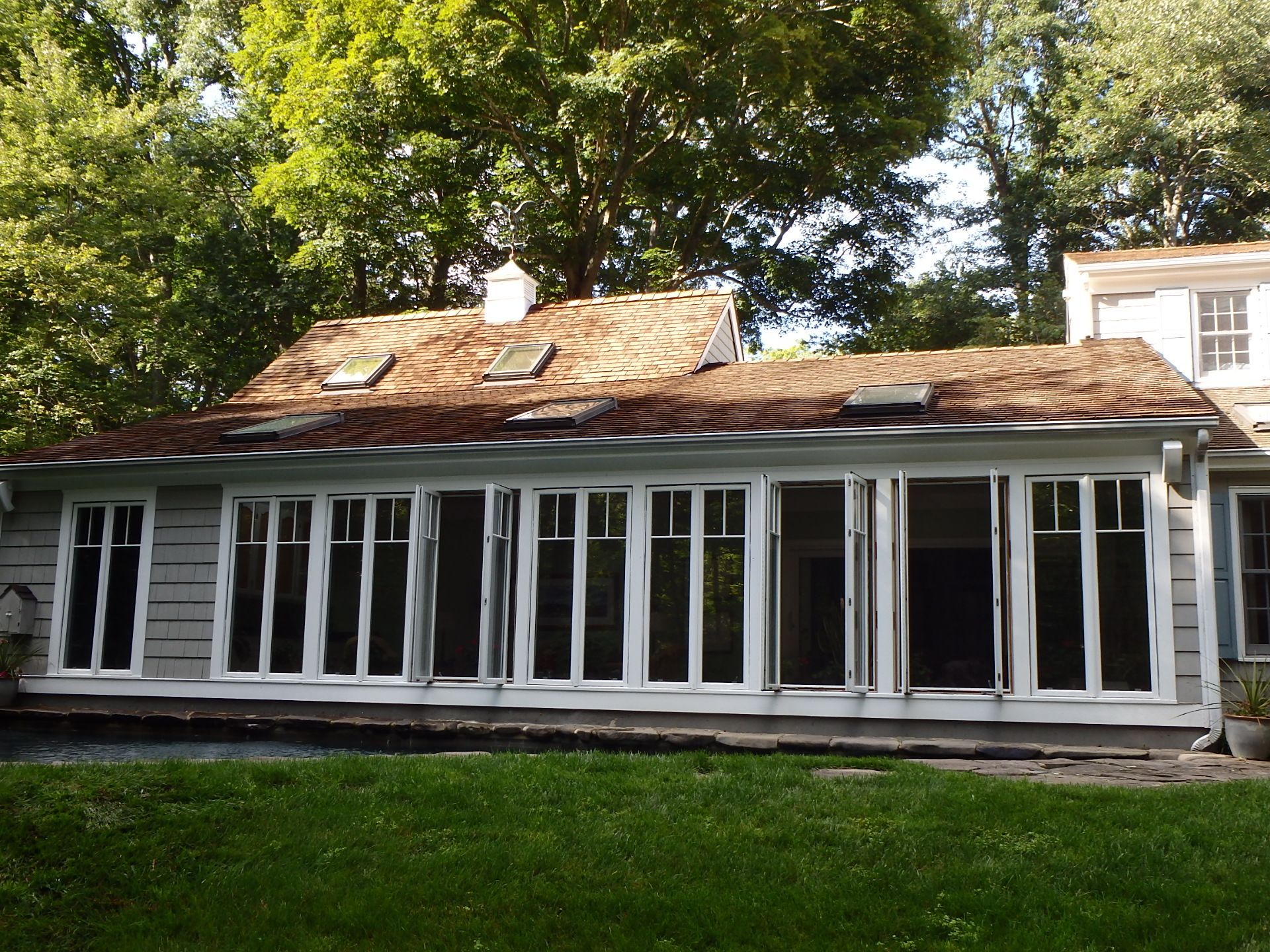 One-story house with a long screened porch, dark exterior trim, and a shingled roof under trees.
