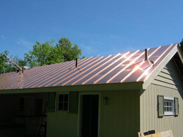 Small green house with a shiny copper-colored metal roof under a blue sky