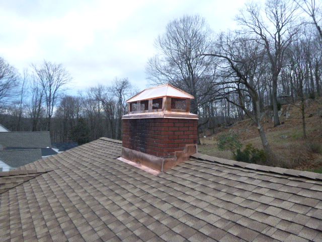 Rooftop with brick chimney and bare trees under a cloudy sky