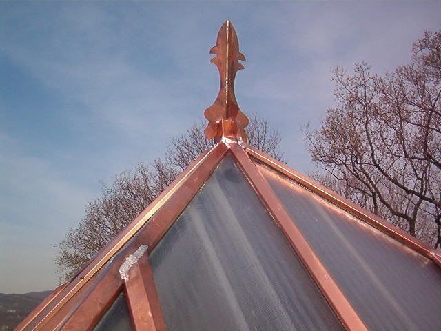 Copper-topped glass roof with a decorative finial against a cloudy sky