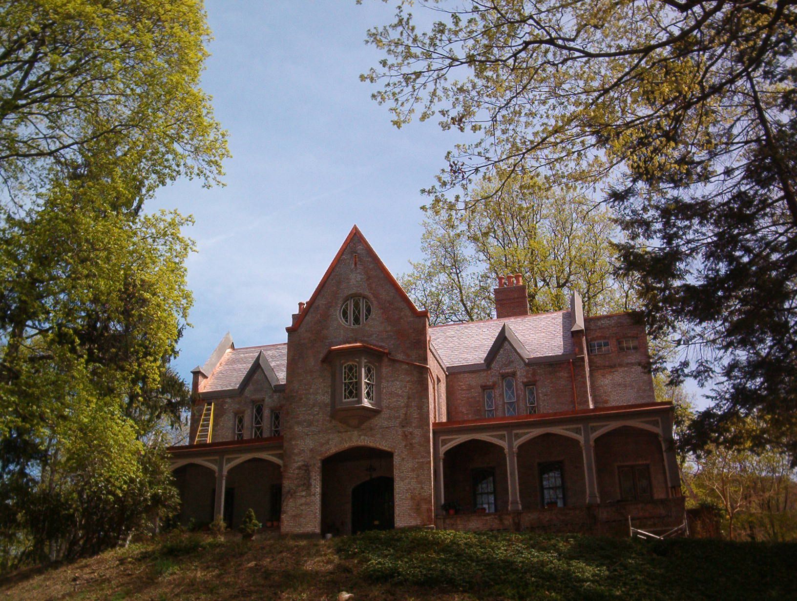 Old red-brick house with arched porch, centered under trees on a sunny day