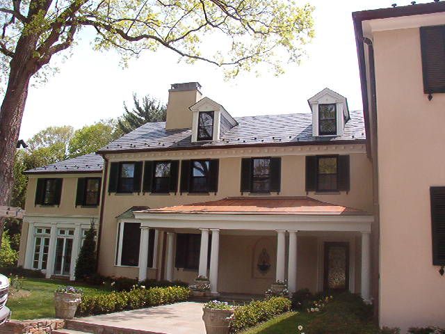 Large beige two-story house with dormer windows, porch, and a tree in the front yard
