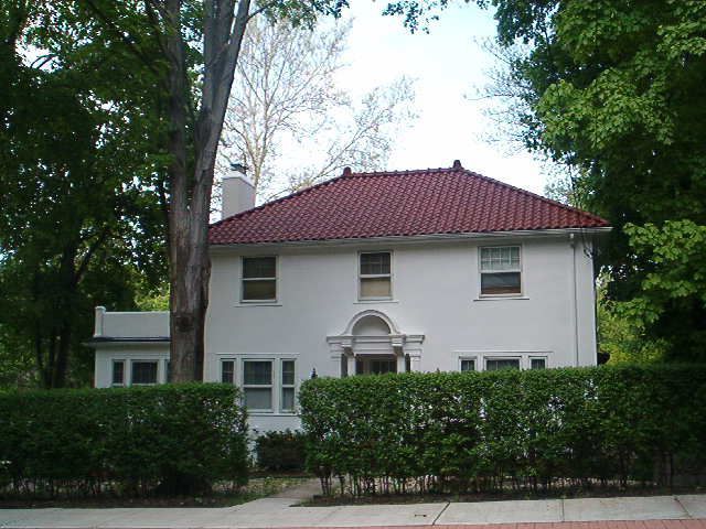 White house with a red tiled roof behind hedges and trees