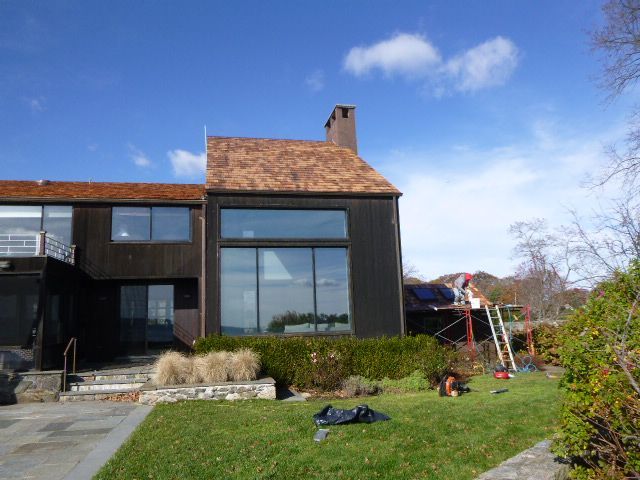 Modern house with black siding, large windows, and a grassy yard under a blue sky