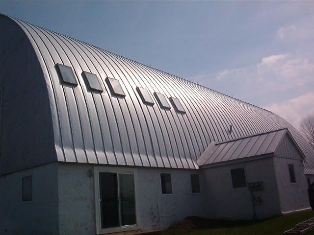 Small white building with a curved metal roof and skylights under a cloudy sky