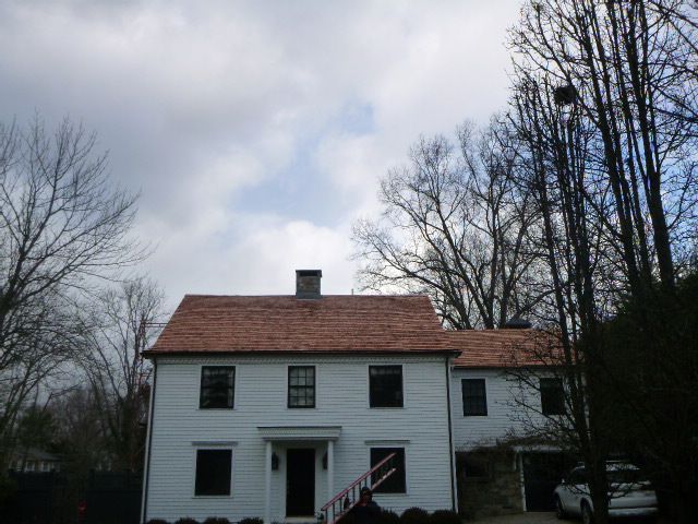White two-story house with a red roof and bare trees under a cloudy sky