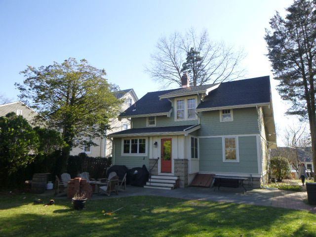 Gray two-story house with a porch, white trim, and a red front door, surrounded by trees and lawn.