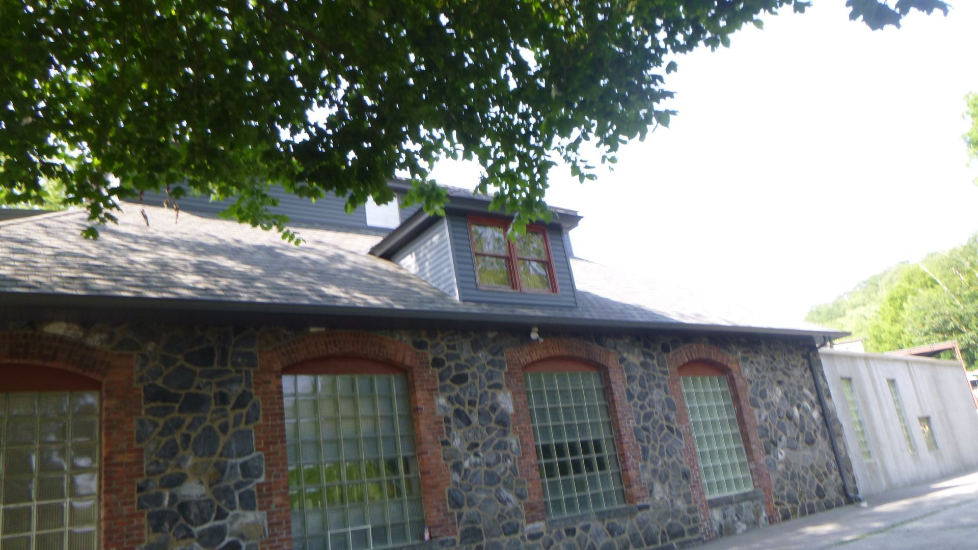 Stone building with arched windows and dormer roof under trees, in bright daylight