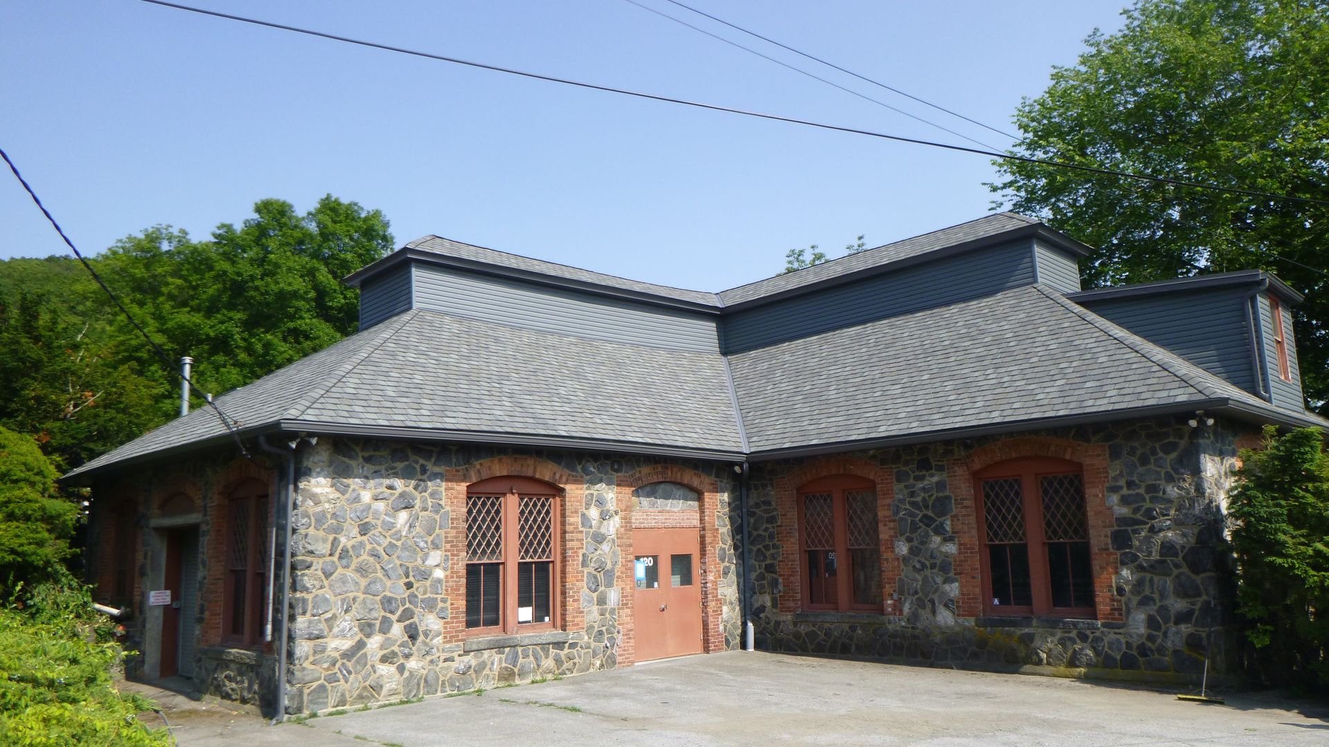 Stone building with red-framed windows and a gray metal roof under a clear blue sky