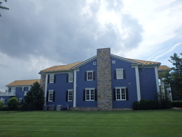 Blue two-story house with white trim and a stone chimney, seen from a lawn under cloudy sky