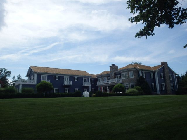 Large dark-blue mansion with white trim on a green lawn under a cloudy sky