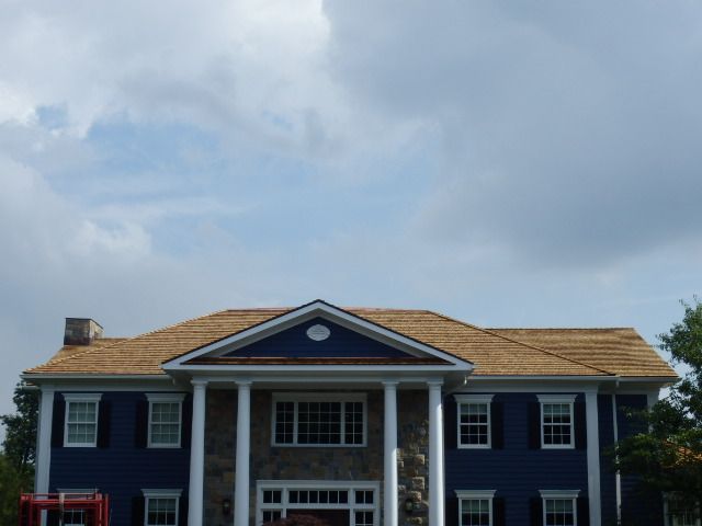 A blue house with white columns and a tan roof under a cloudy sky.