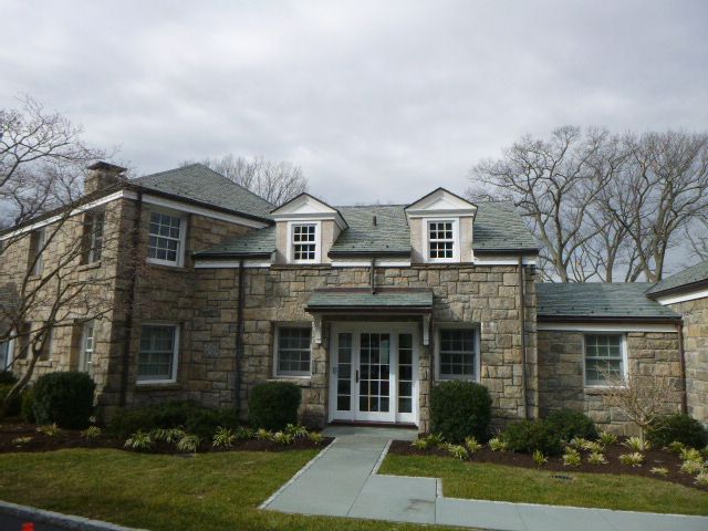 Stone house with dormer windows, front porch, and a walkway in a cloudy yard
