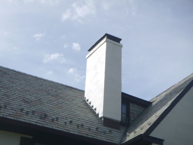 White chimney on a dark shingled roof against a blue sky