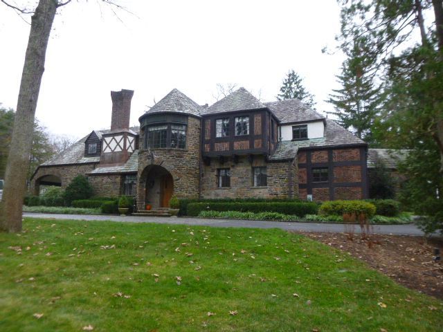 Stone mansion with arched entrance, dark-trimmed windows, and a green lawn in front