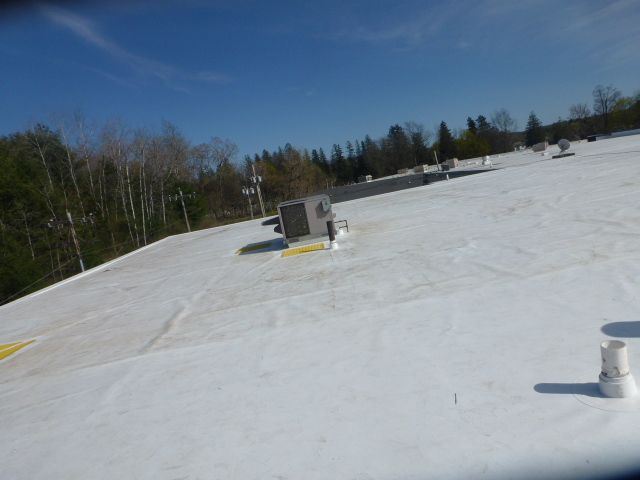 Flat white rooftop with vents and a small rooftop unit under a clear blue sky